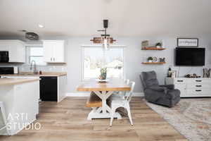 Kitchen with black appliances, decorative light fixtures, white cabinetry, and light wood-type flooring