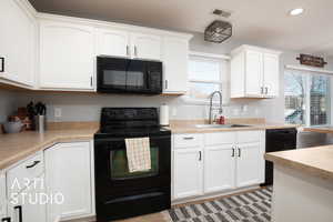 Kitchen featuring sink, white cabinetry, and black appliances