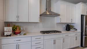 Kitchen with white cabinetry, wall chimney exhaust hood, stainless steel appliances, and decorative backsplash