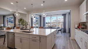 Kitchen featuring pendant lighting, sink, appliances with stainless steel finishes, a kitchen island with sink, and white cabinetry