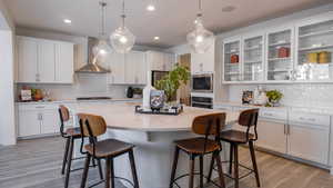 Kitchen with a kitchen island, built in microwave, white cabinetry, oven, and wall chimney exhaust hood