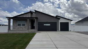 Contemporary house with a front lawn, driveway, stone siding, an attached garage, and fence