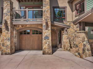 View of exterior entry with concrete driveway, stone siding, a balcony, an attached garage, and stucco siding