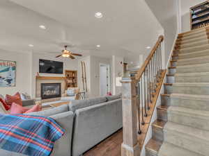 Living area with recessed lighting, dark wood-style flooring, stairs, a glass covered fireplace, and ceiling fan