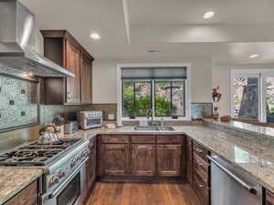 Kitchen with wall chimney exhaust hood, a sink, stainless steel appliances, dark wood-style floors, and light stone countertops
