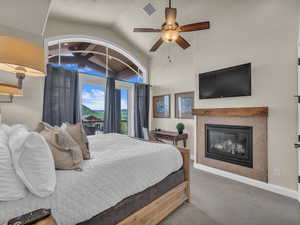 Carpeted bedroom featuring lofted ceiling, a tile fireplace, baseboards, and ceiling fan