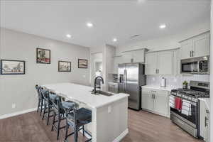 Kitchen featuring sink, a breakfast bar, appliances with stainless steel finishes, a center island with sink, and decorative backsplash