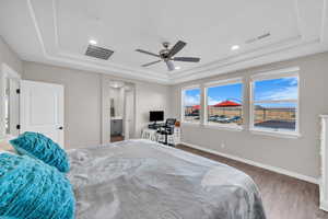 Bedroom with ensuite bath, dark hardwood / wood-style floors, ceiling fan, and a tray ceiling