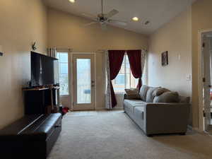 Living room with ceiling fan, light colored carpet, and vaulted ceiling