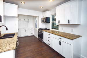 Kitchen featuring appliances with stainless steel finishes, sink, white cabinets, dark hardwood / wood-style flooring, and light stone counters