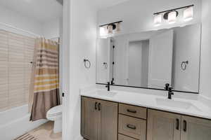 Full bathroom featuring toilet, vanity, and shower / bathtub combination with curtain