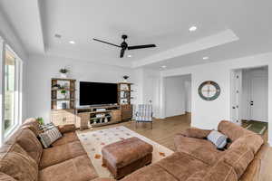 Living room with light hardwood / wood-style floors, a raised ceiling, and ceiling fan