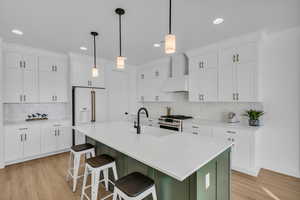 Kitchen with white cabinetry, wall chimney exhaust hood, sink, and premium appliances