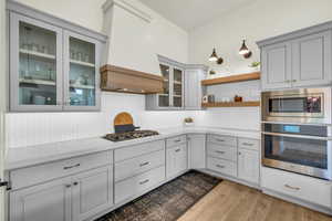 Kitchen featuring gray cabinets, premium range hood, appliances with stainless steel finishes, tasteful backsplash, and light hardwood / wood-style floors