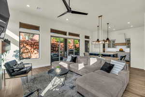 Living room with ceiling fan, a towering ceiling, and light wood-type flooring