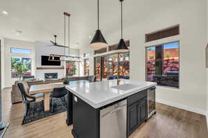 Kitchen with decorative light fixtures, stainless steel dishwasher, a large fireplace, a kitchen island with sink, and light hardwood / wood-style floors