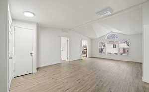 Unfurnished living room featuring lofted ceiling and light hardwood / wood-style flooring