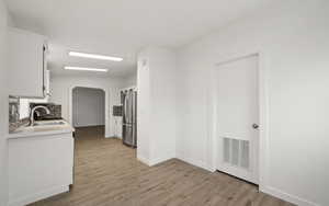 Kitchen with tasteful backsplash, sink, white cabinets, stainless steel fridge, and light wood-type flooring