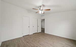 Unfurnished bedroom with ceiling fan, light hardwood / wood-style floors, and multiple closets