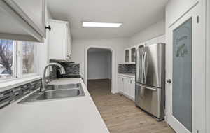 Kitchen featuring stainless steel refrigerator, sink, white cabinets, decorative backsplash, and light wood-type flooring