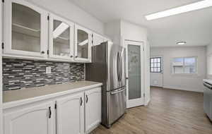 Kitchen featuring white cabinetry, backsplash, light hardwood / wood-style floors, and stainless steel refrigerator