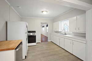 Kitchen with white cabinetry, ornamental molding, white fridge, and range with gas cooktop