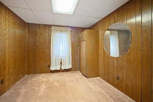 Empty room featuring a paneled ceiling, wooden walls, and carpet floors