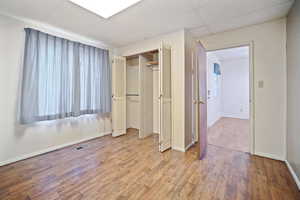 Unfurnished bedroom featuring a drop ceiling, light hardwood / wood-style floors, and a closet