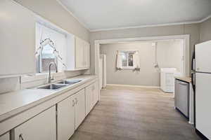 Kitchen featuring washer / dryer, sink, stainless steel dishwasher, white fridge, and white cabinets