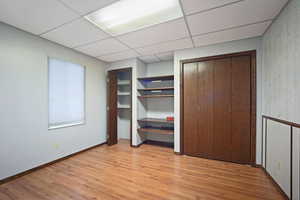 Unfurnished bedroom with a drop ceiling, light hardwood / wood-style floors, and multiple closets