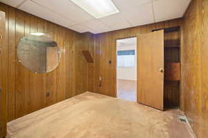 Spare room with a drop ceiling, carpet, and wood walls