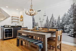 Dining room with ornamental molding, indoor wet bar, beverage cooler, and light wood-type flooring