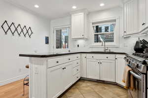 Kitchen featuring stainless steel range oven, sink, kitchen peninsula, decorative backsplash, and white cabinets