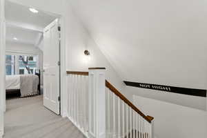 Corridor featuring vaulted ceiling and light carpet