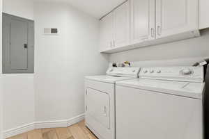 Clothes washing area featuring cabinets, separate washer and dryer, electric panel, and light wood-type flooring