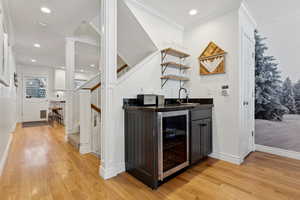 Bar featuring sink, wine cooler, ornamental molding, light wood-type flooring, and ornate columns