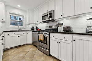 Kitchen featuring light tile patterned flooring, sink, appliances with stainless steel finishes, decorative backsplash, and white cabinets