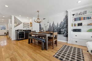 Dining room with wine cooler, ornamental molding, light hardwood / wood-style floors, and indoor wet bar