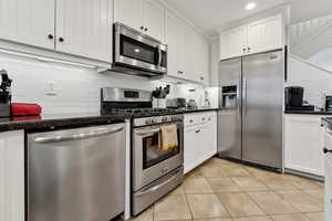 Kitchen featuring light tile patterned flooring, white cabinets, dark stone counters, decorative backsplash, and stainless steel appliances