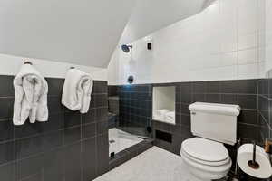 Bathroom with lofted ceiling, a shower with door, tile walls, and toilet