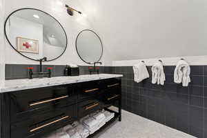 Bathroom featuring vanity, vaulted ceiling, and tile walls