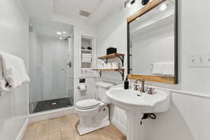 Bathroom with built in shelves, sink, an enclosed shower, and toilet