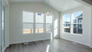 Unfurnished dining area featuring vaulted ceiling, hardwood / wood-style floors, and a notable chandelier