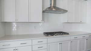 Kitchen with wall chimney range hood, backsplash, stainless steel gas stovetop, and white cabinets