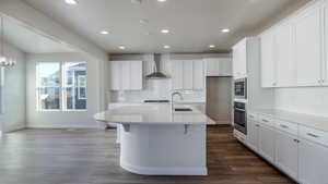 Kitchen with white cabinetry, wall chimney range hood, sink, and stainless steel oven