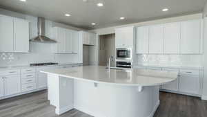 Kitchen with sink, appliances with stainless steel finishes, a kitchen island with sink, white cabinetry, and wall chimney exhaust hood