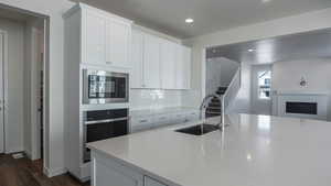 Kitchen featuring built in microwave, sink, white cabinets, backsplash, and stainless steel oven