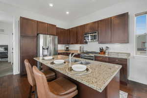 Kitchen featuring a kitchen island with sink, sink, light stone counters, and stainless steel appliances