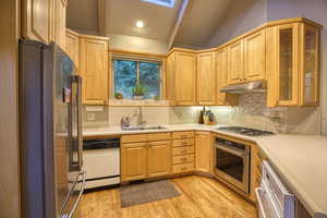 Kitchen with sink, light hardwood / wood-style flooring, stainless steel appliances, decorative backsplash, and light brown cabinets