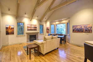 Living room featuring beam ceiling, high vaulted ceiling, a tile fireplace, and light wood-type flooring